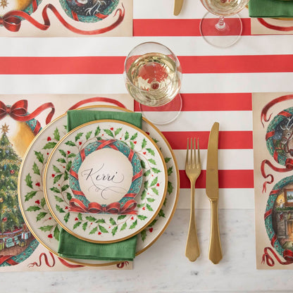 An elegant Christmas themed table setting with the Red Classic Stripe Runner underneath holly rimmed plates and O Christmas Tree Wreath Place Card with the name &quot;Kerri&quot; written on it.