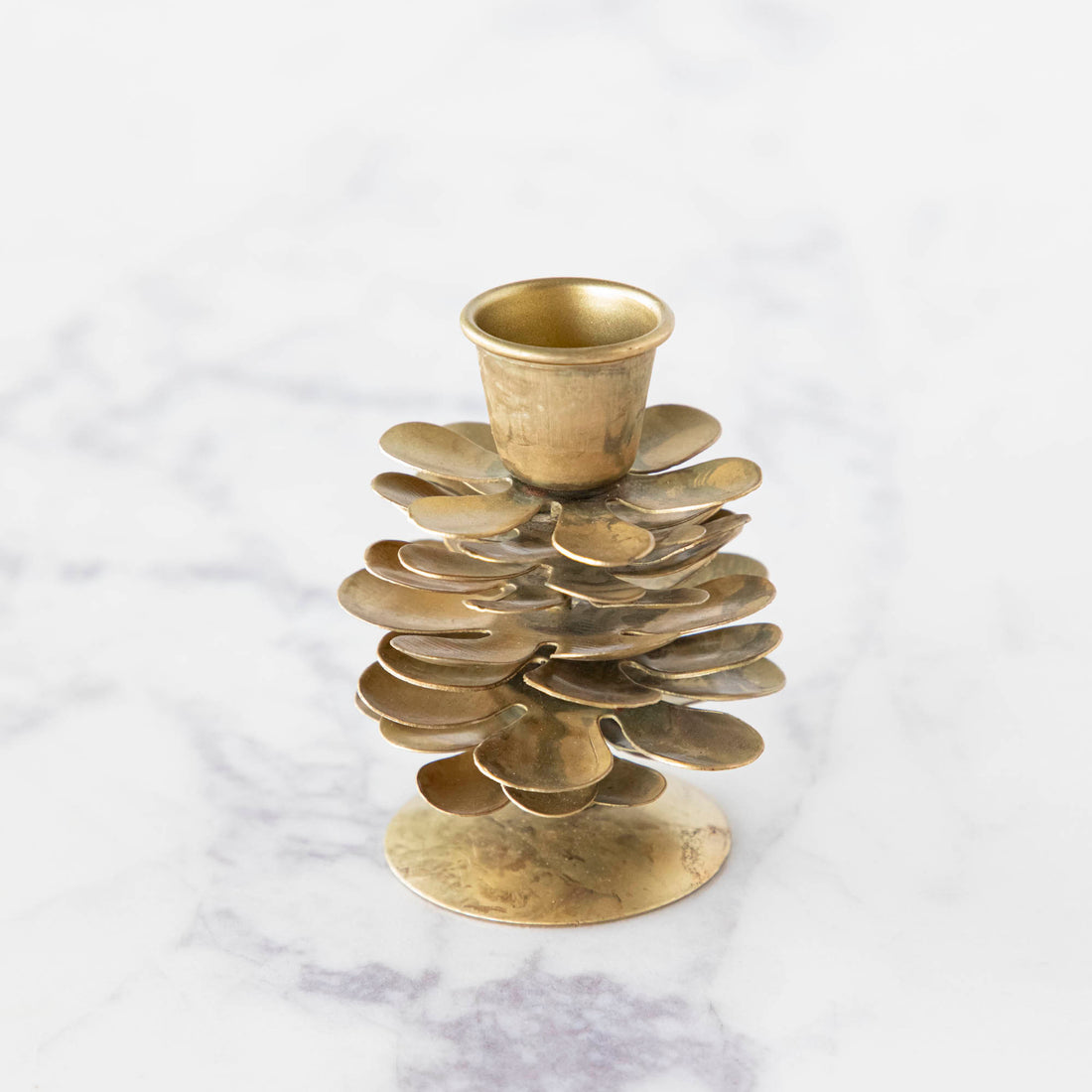 An iron, Gold Crackle Candle Holder, shaped like a pinecone with a hole for a taper candle, on a marble table.