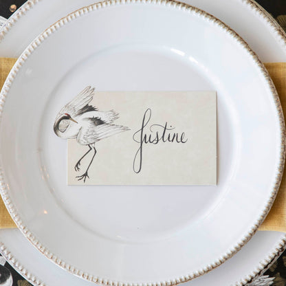 Crane Dance Place Card with &quot;Justine&quot; written on it, laying flat on a set of dinner plates.