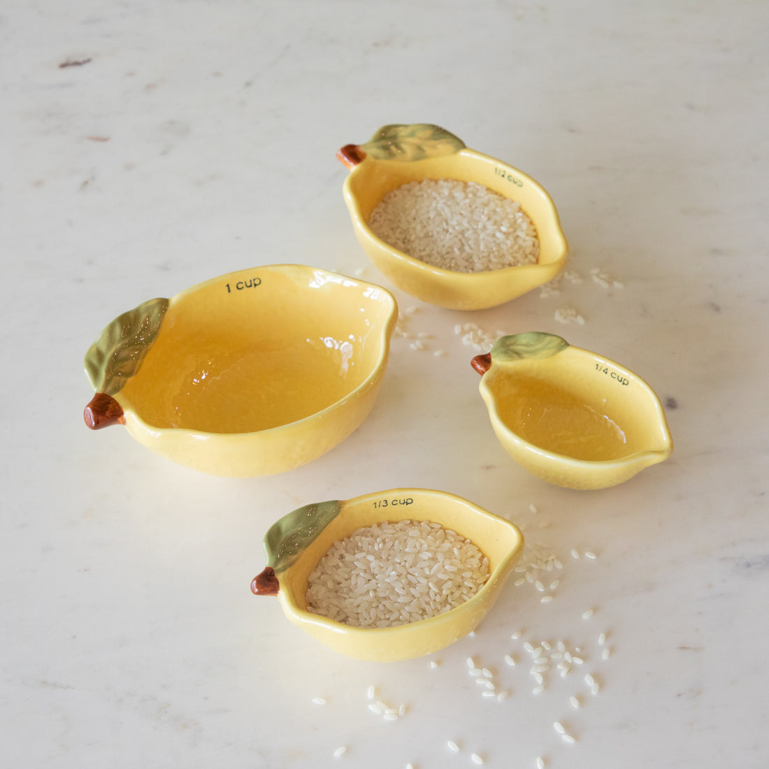 Stoneware Lemon Measuring Cups, Set of 4 with rice in two of the cups and some grains scattered on the table.