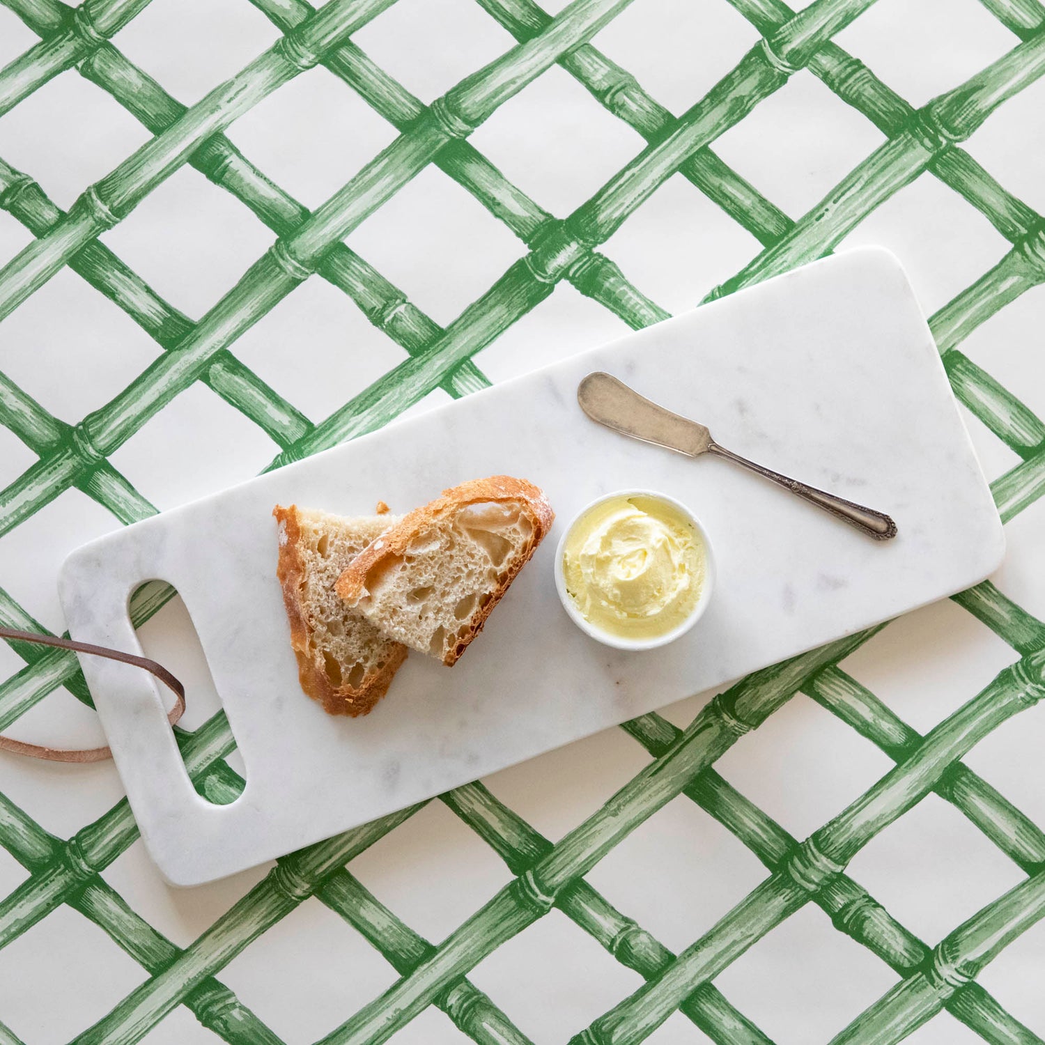 A White Marble Cheese Board with sliced bread and butter and a butter spreader on top, on a green lattice runner.