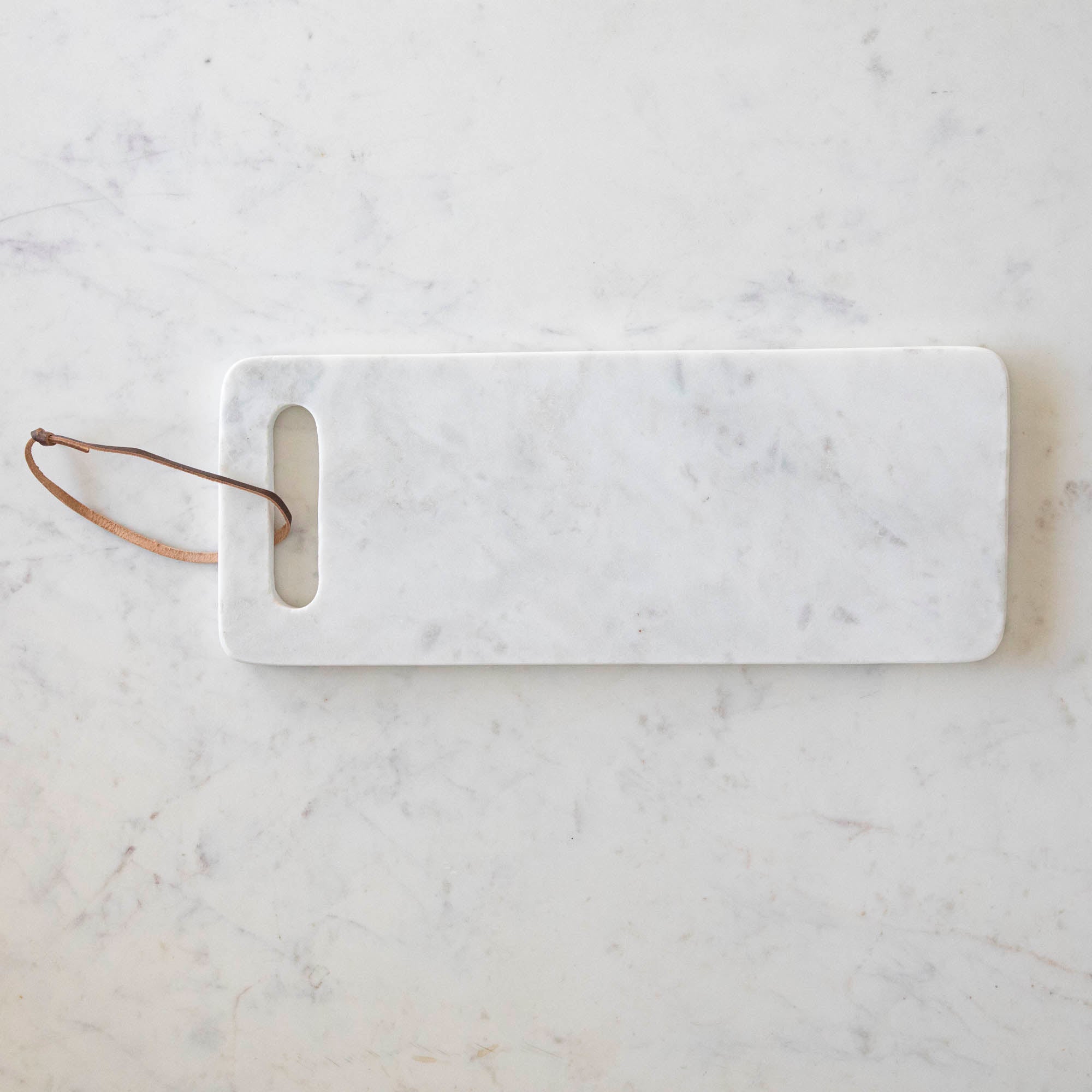 A White Marble Cheese Board  with a cutout made for holding and a brown loop for decoration.