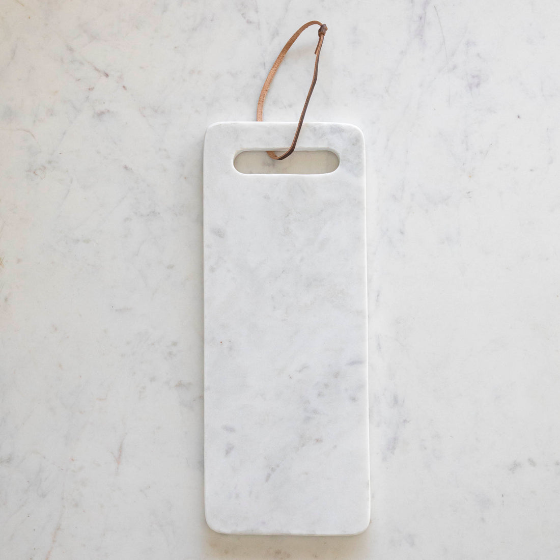 A White Marble Cheese Board  with a cutout made for holding and a brown loop for decoration.