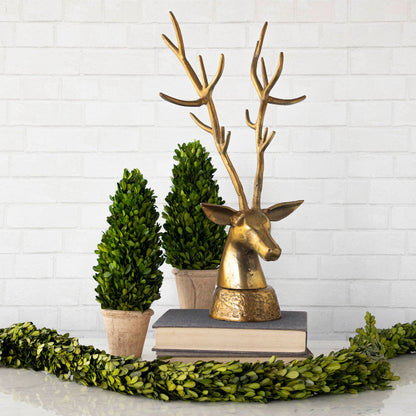 A rustic, metal Deer head on a stack of books, surrounded by boxwood.