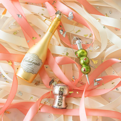 Three Olives Please Ornament, Cheers Cork Ornament and Congratulations Gold Champagne Ornament amongst ribbons and confetti.