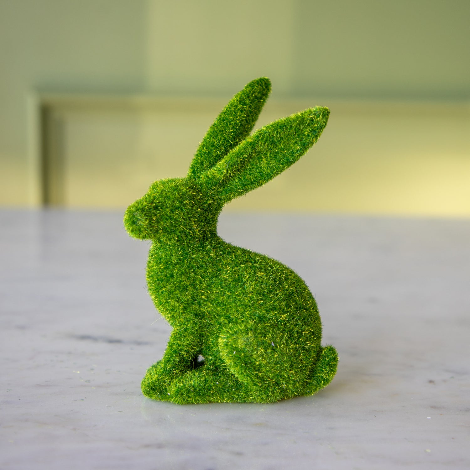 The side view of the large green flocked bunny perched up looking to the side.