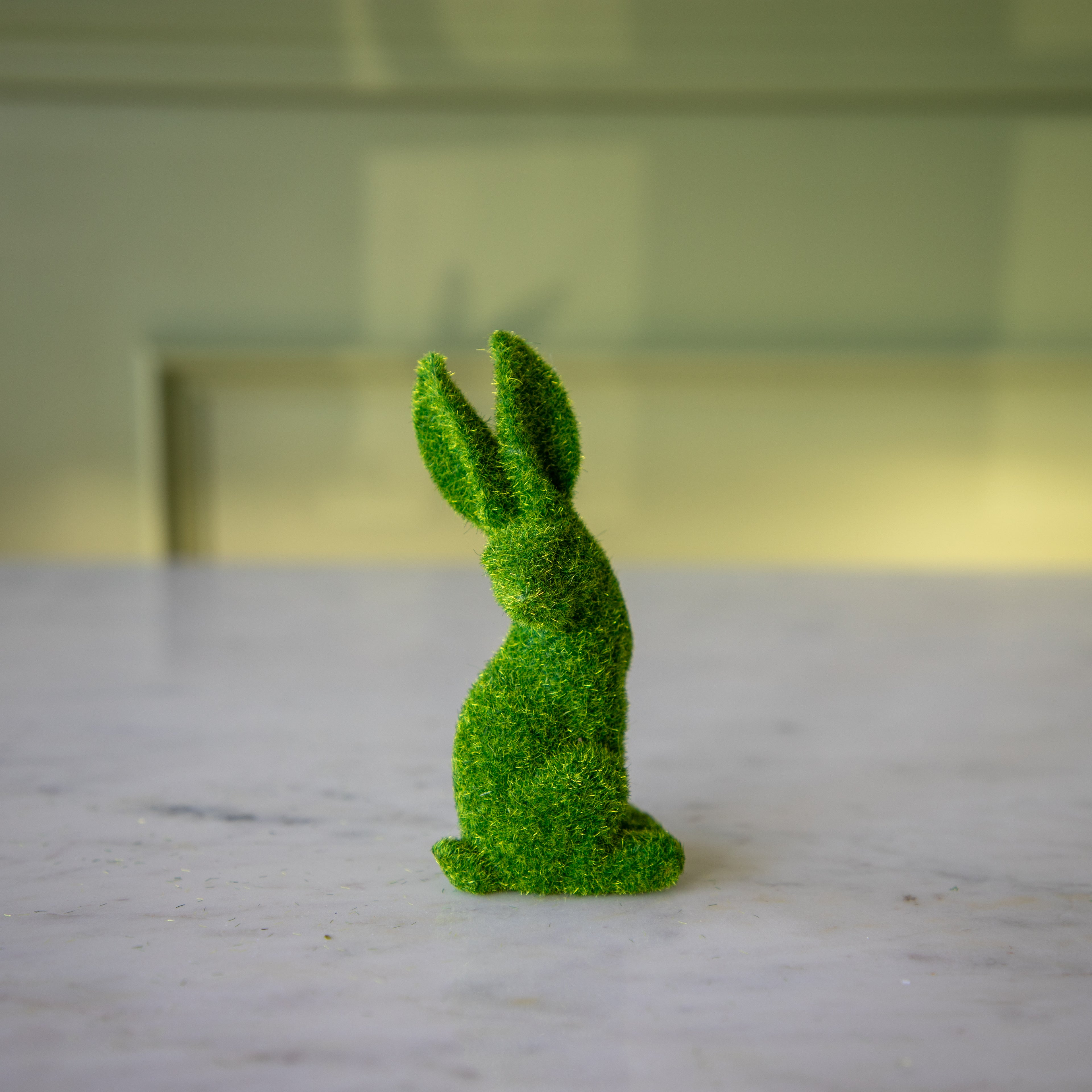 The side view of the small green flocked bunny looking over its shoulder with its ears perked up.