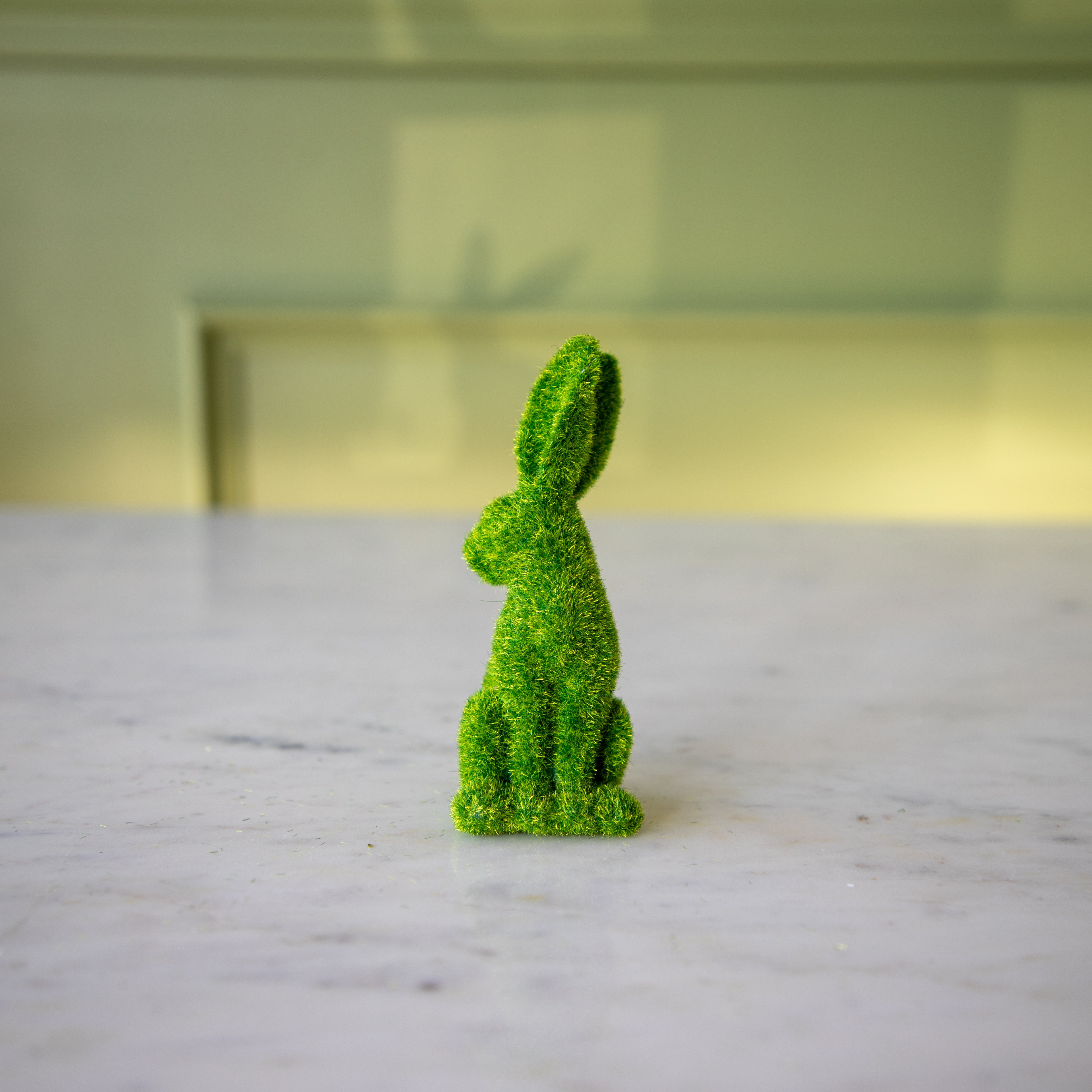 The front view of the small green flocked bunny looking over its shoulder with his ears perked up.