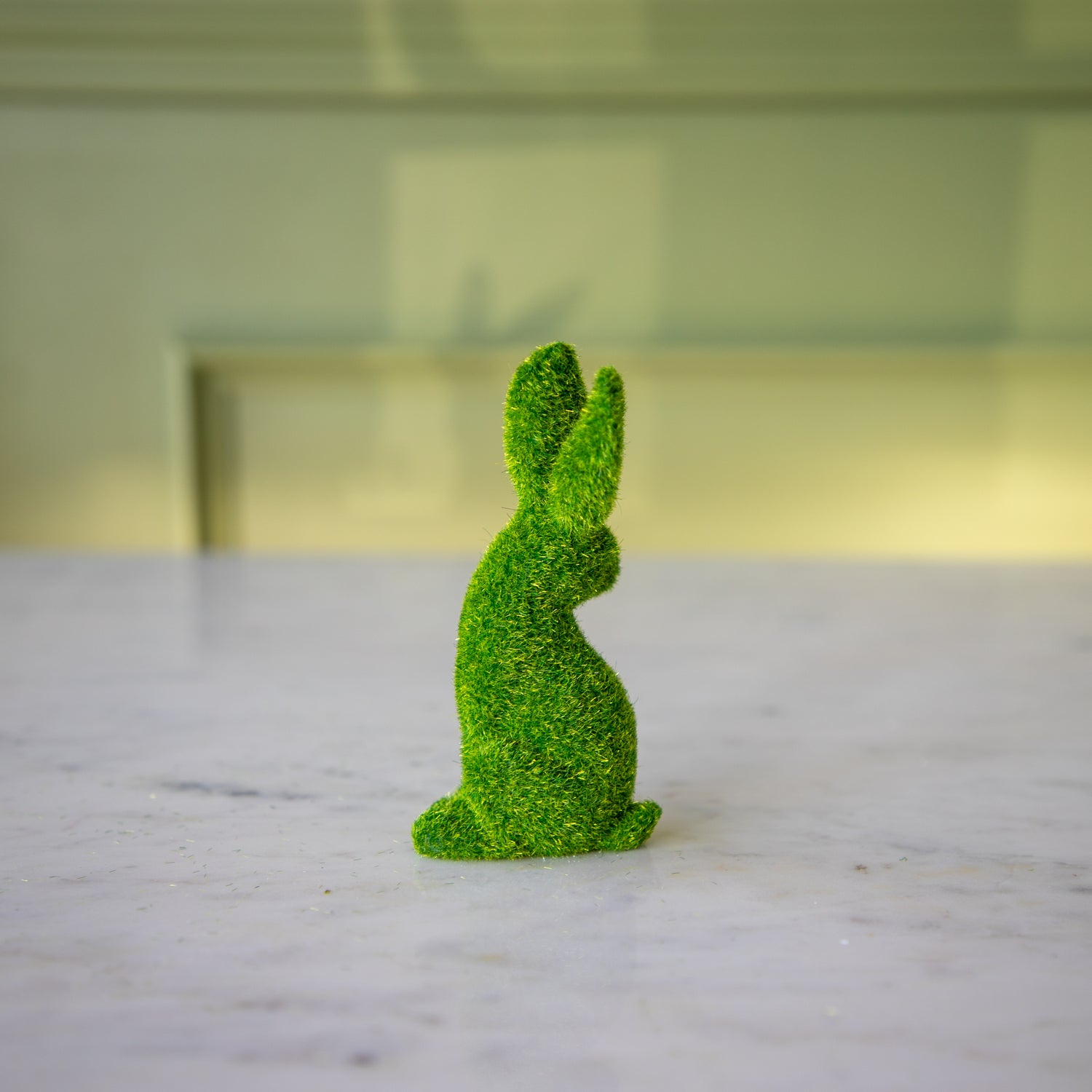 The side view of the small green flocked bunny looking over its shoulder with its ears perked up.