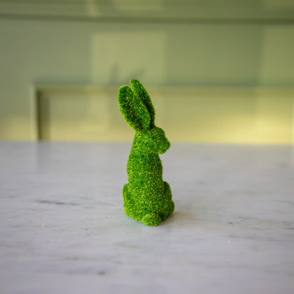 The back view of the small green flocked bunny looking over its shoulder with its ears perked up.