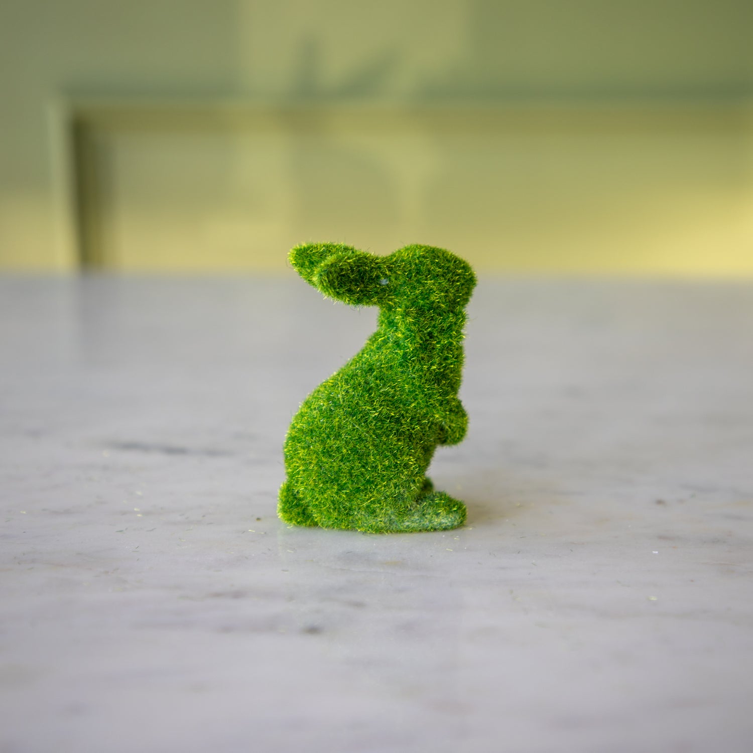 The side view of the extra small green flocked bunny on its hind legs and ears all the way back.