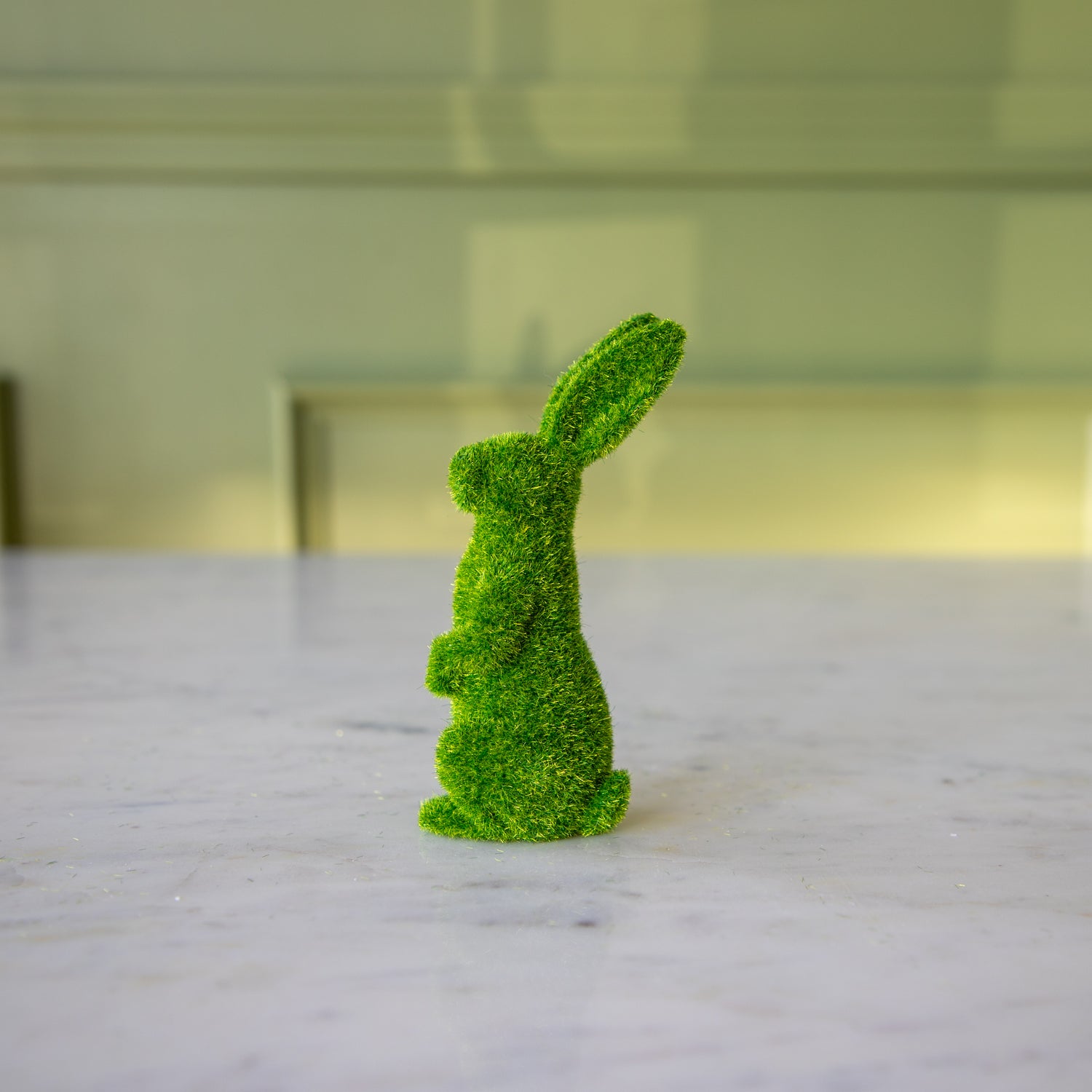 The side view of the medium green flocked bunny on its hind legs looking to the side.