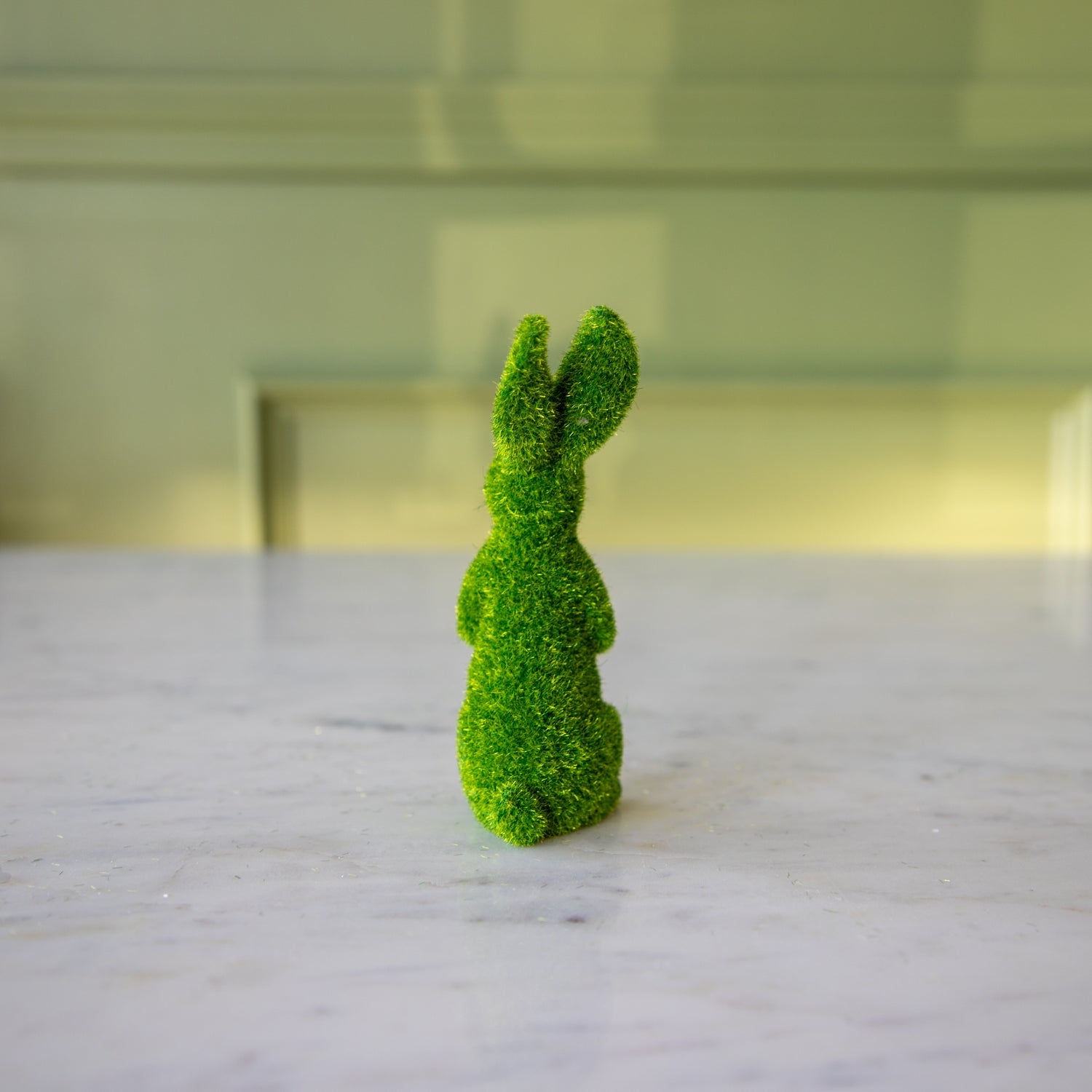 The back view of the medium green flocked bunny on its hind legs looking to the side.