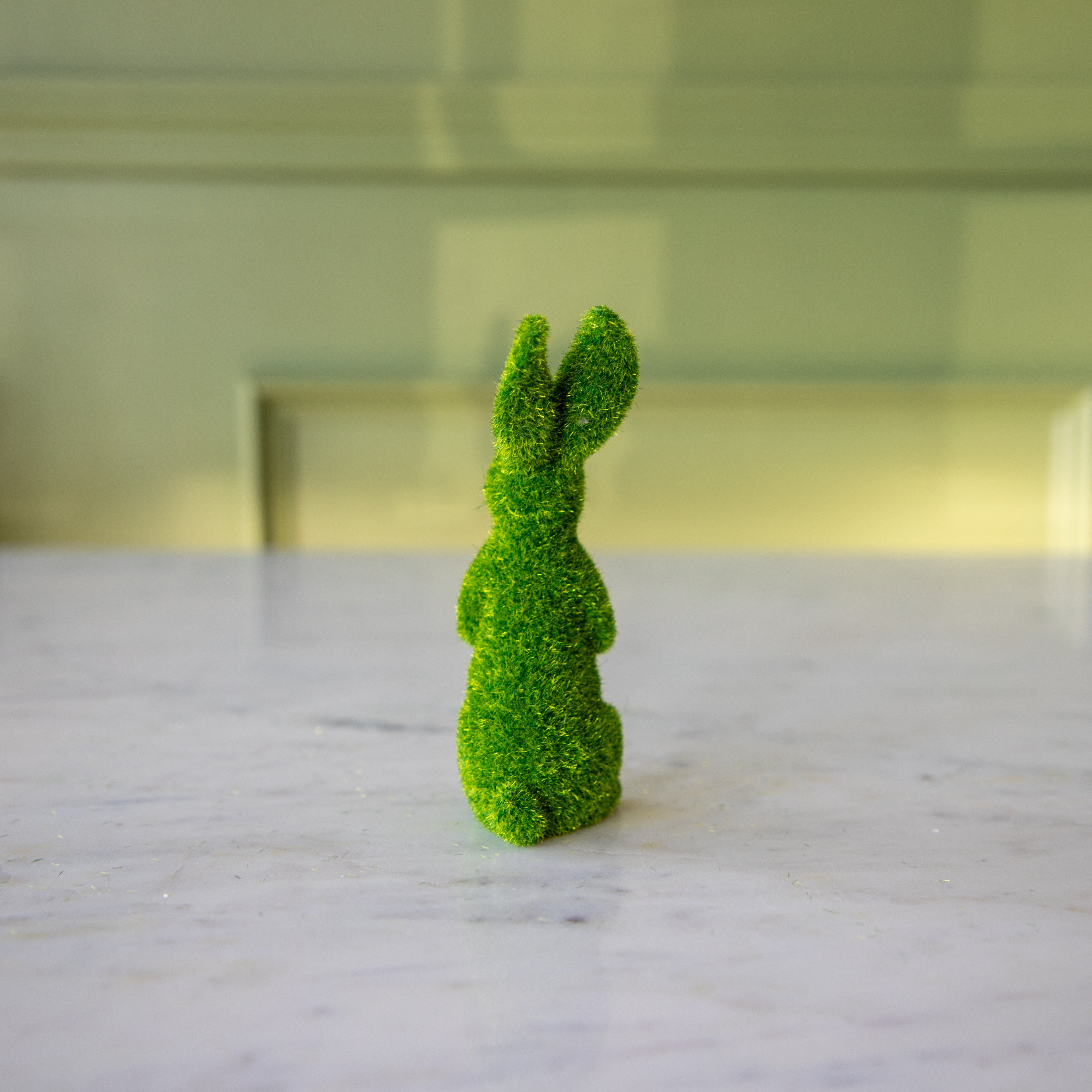 The back view of the medium green flocked bunny on its hind legs looking to the side.