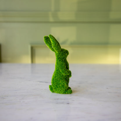 The side view of the medium green flocked bunny on its hind legs looking to the side.