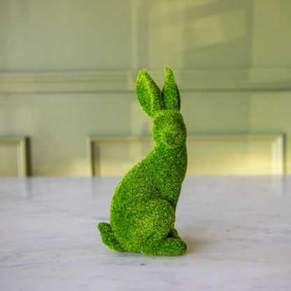 The side view of the extra large green flocked bunny sitting up, looking over its shoulder towards the front.