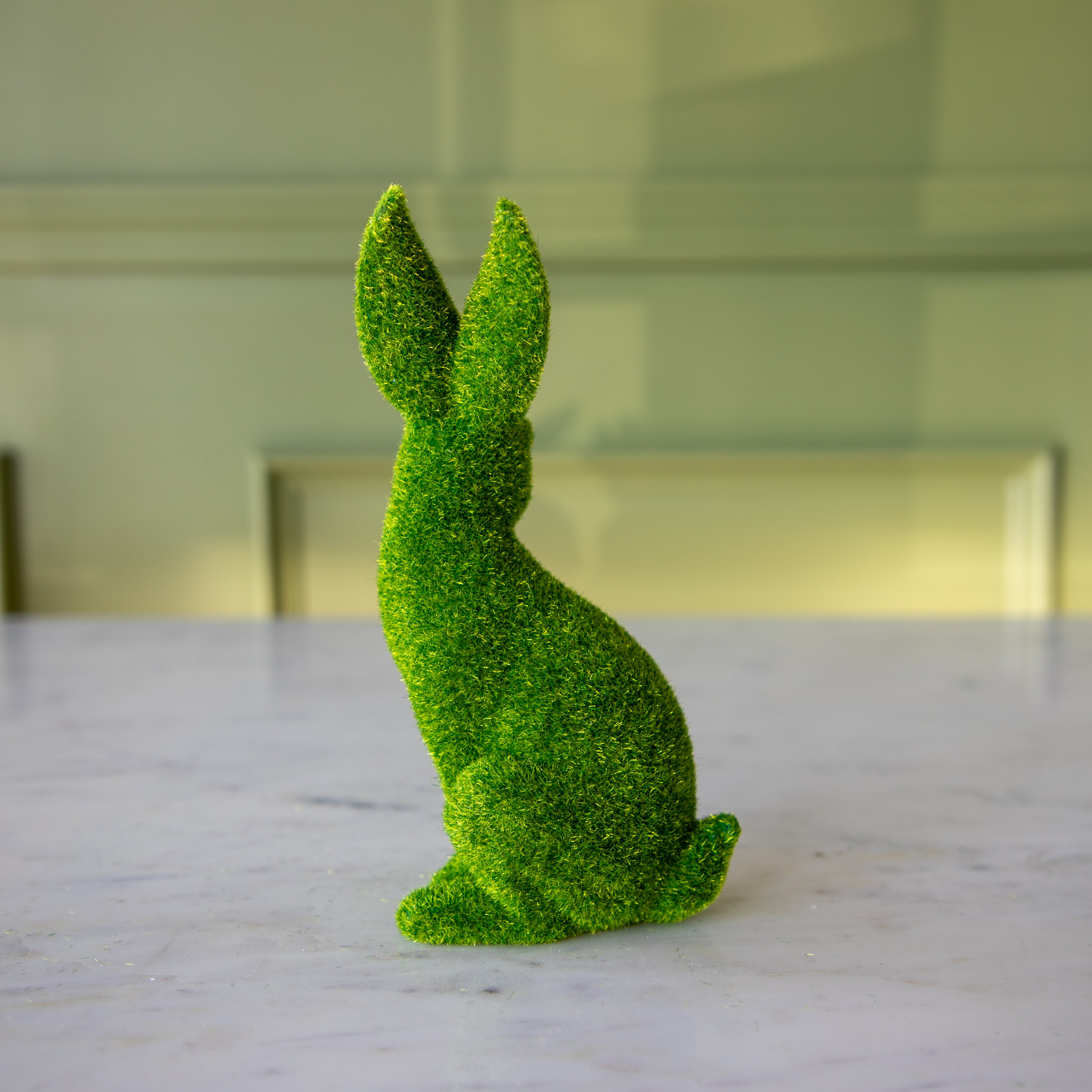 The side view of the extra large green flocked bunny sitting up, looking over its shoulder.