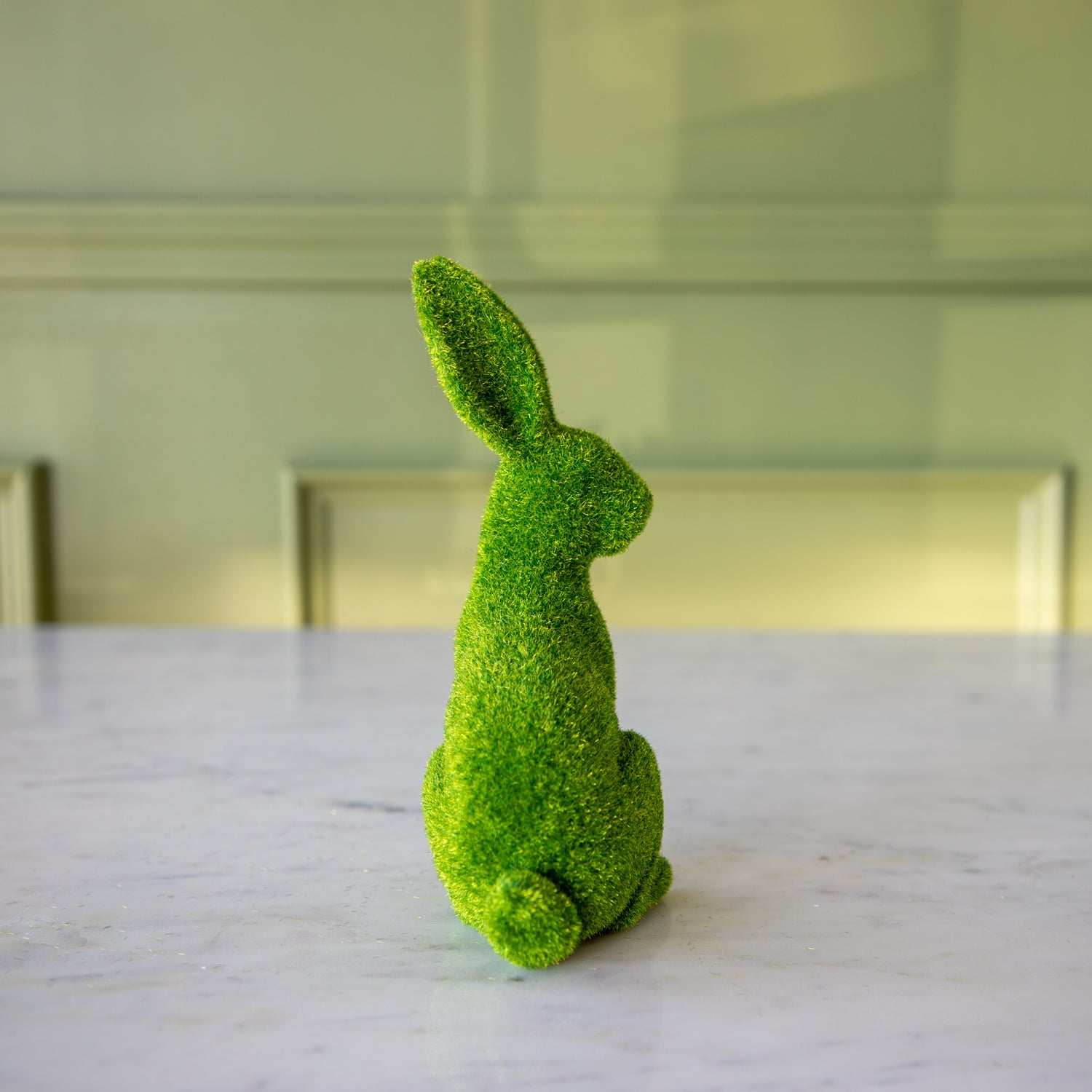 The back view of the extra large green flocked bunny sitting up, looking over its shoulder.