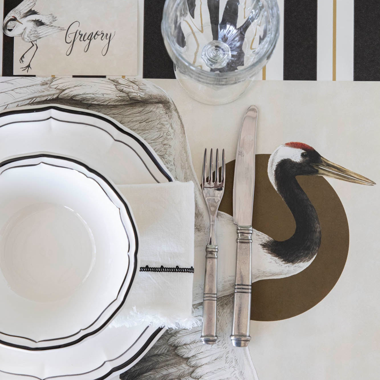 Eastern Crane Placemat on top of the Black &amp; Gold Awning Stripe Runner, on an elegantly styled table.