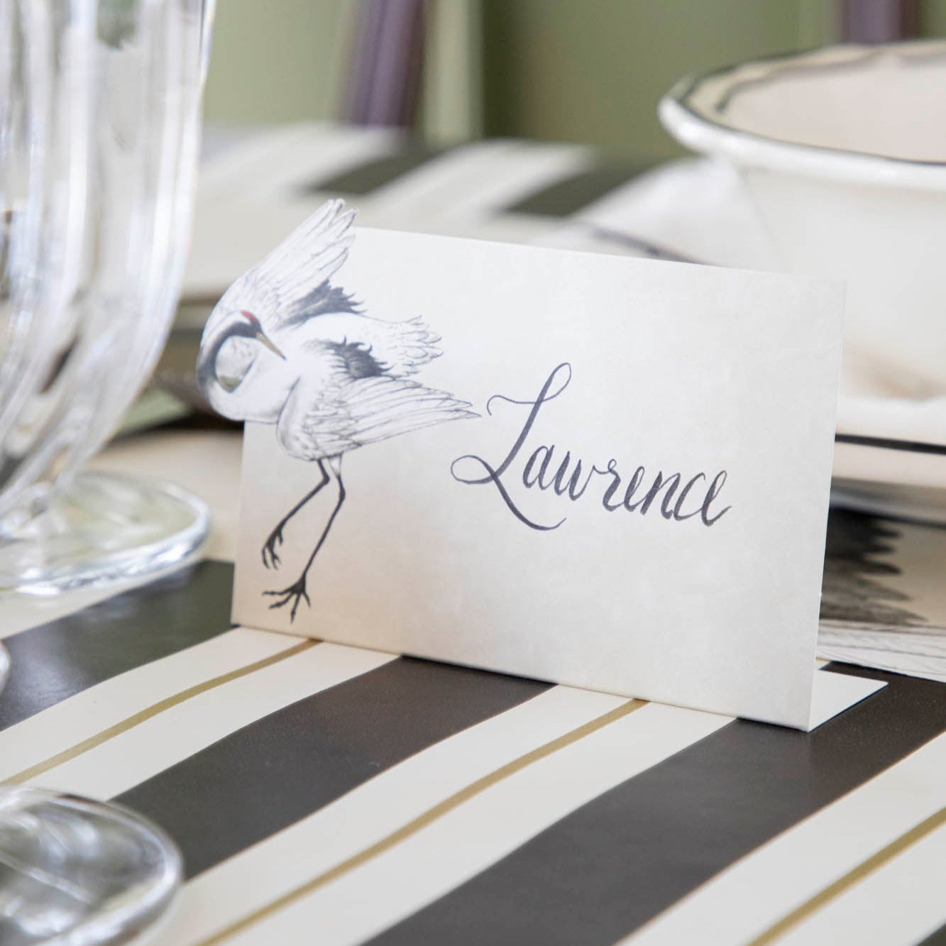 Crane Place Card with &quot;Lawrence&quot; written on it, behind an elegantly styled place setting for one.