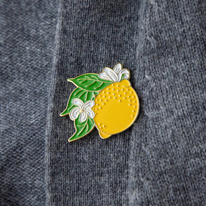 A Lemon Enamel Pin from Hester &amp; Cook adorns the front of a stylish gray sweater.