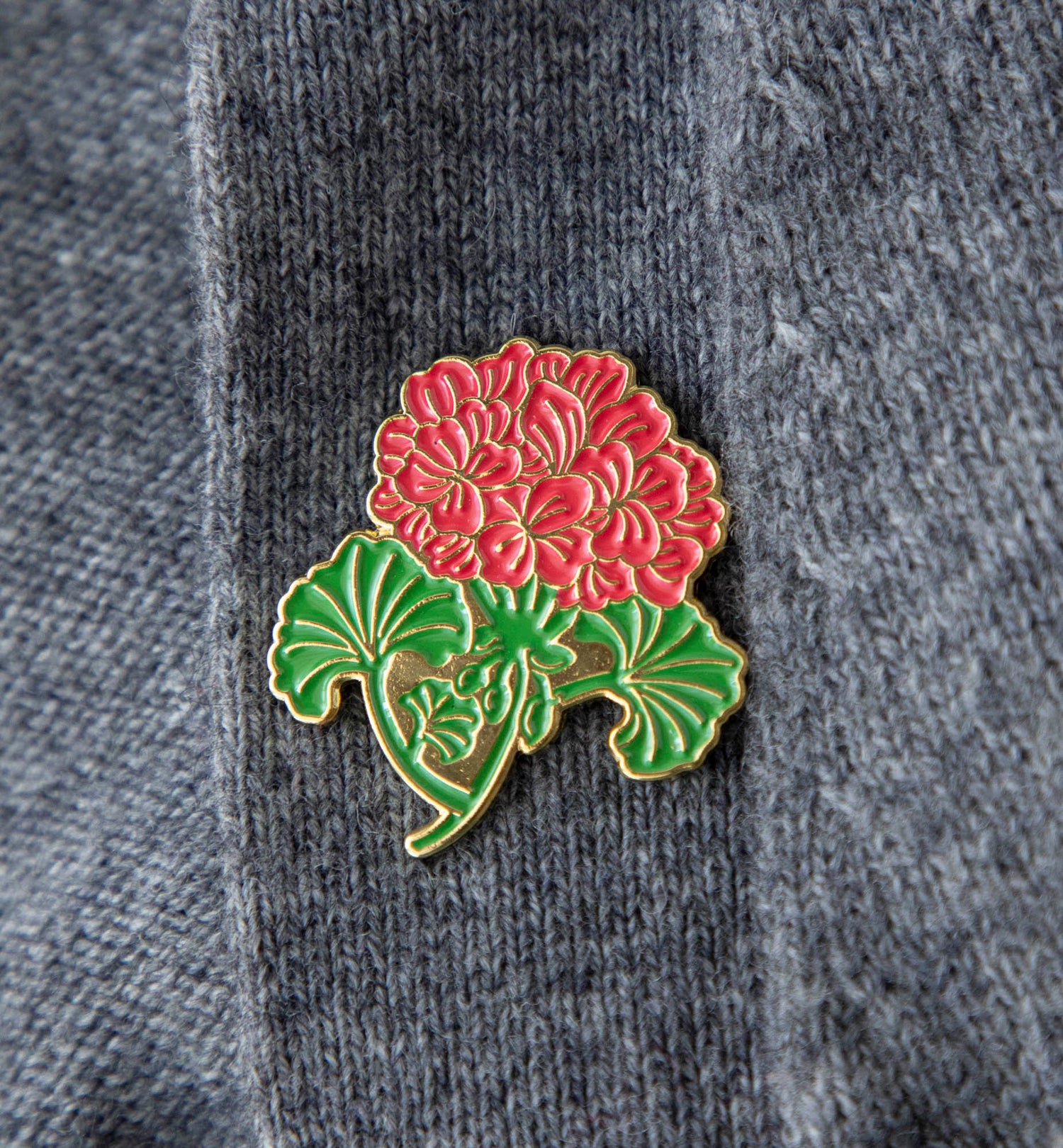 An enchanting Hester &amp; Cook Geranium Enamel Pin with a beautiful red Geranium flower delicately paired with green foliage.