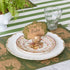 The antique gold finish Owl Name Card Holder, holding the Moss Fable Toile Place Card with "Aiden" written on it, on a table setting with two dinner plates, the Moss Fable Toile Placemat and Moss Green Classic Stripe Runner underneath.