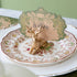 An antique gold finish Deer Place Card Holder on a floral dinner plate, holding the Moss Fable Toile Place Card with the name "Willow" written on it in cursive.