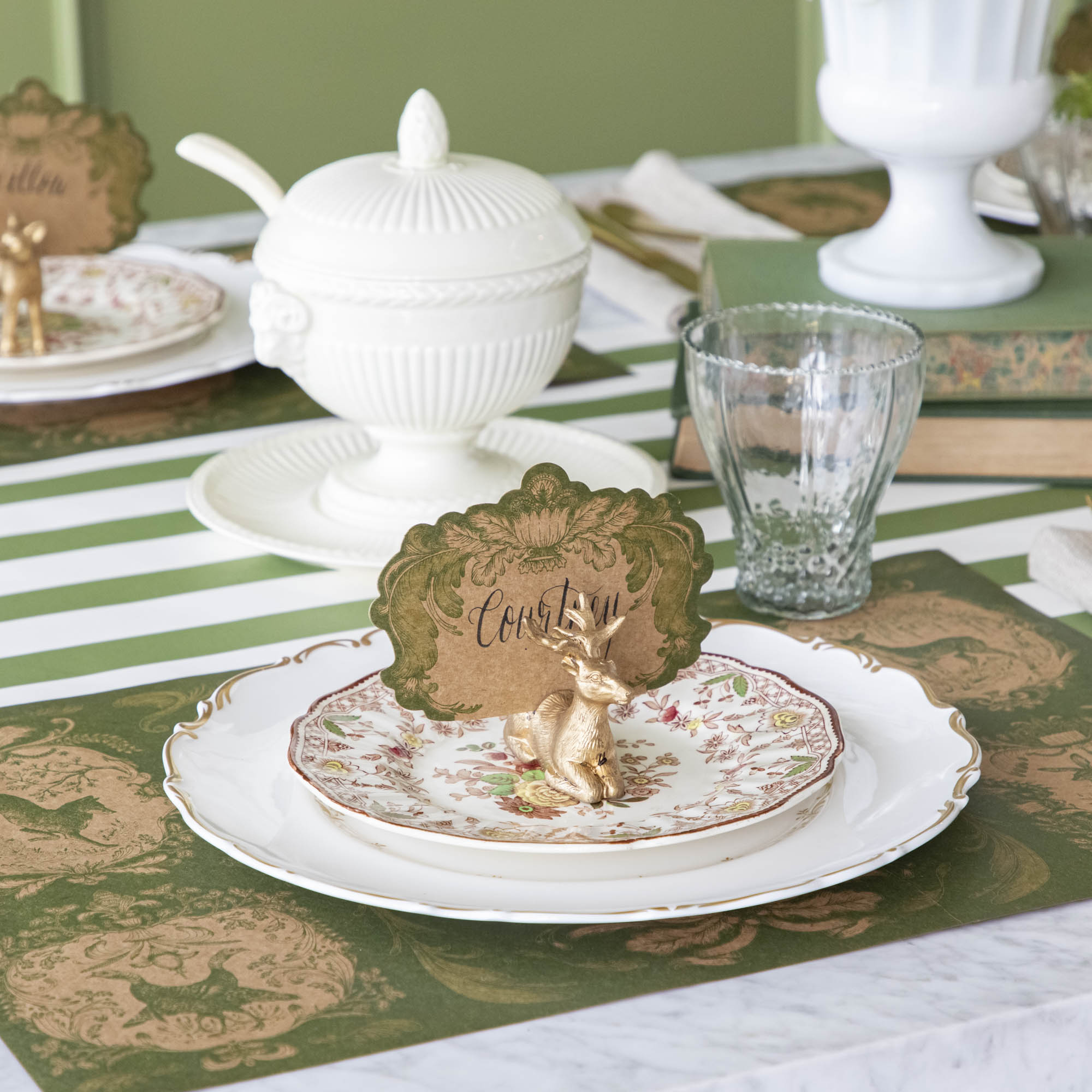 An elegant table setting with the Deer Place Card Holder holding the Moss Fable Toile Place Card with the name &quot;Courtney&quot; written in cursive, and the Moss Fable Toile Placemat underneath.