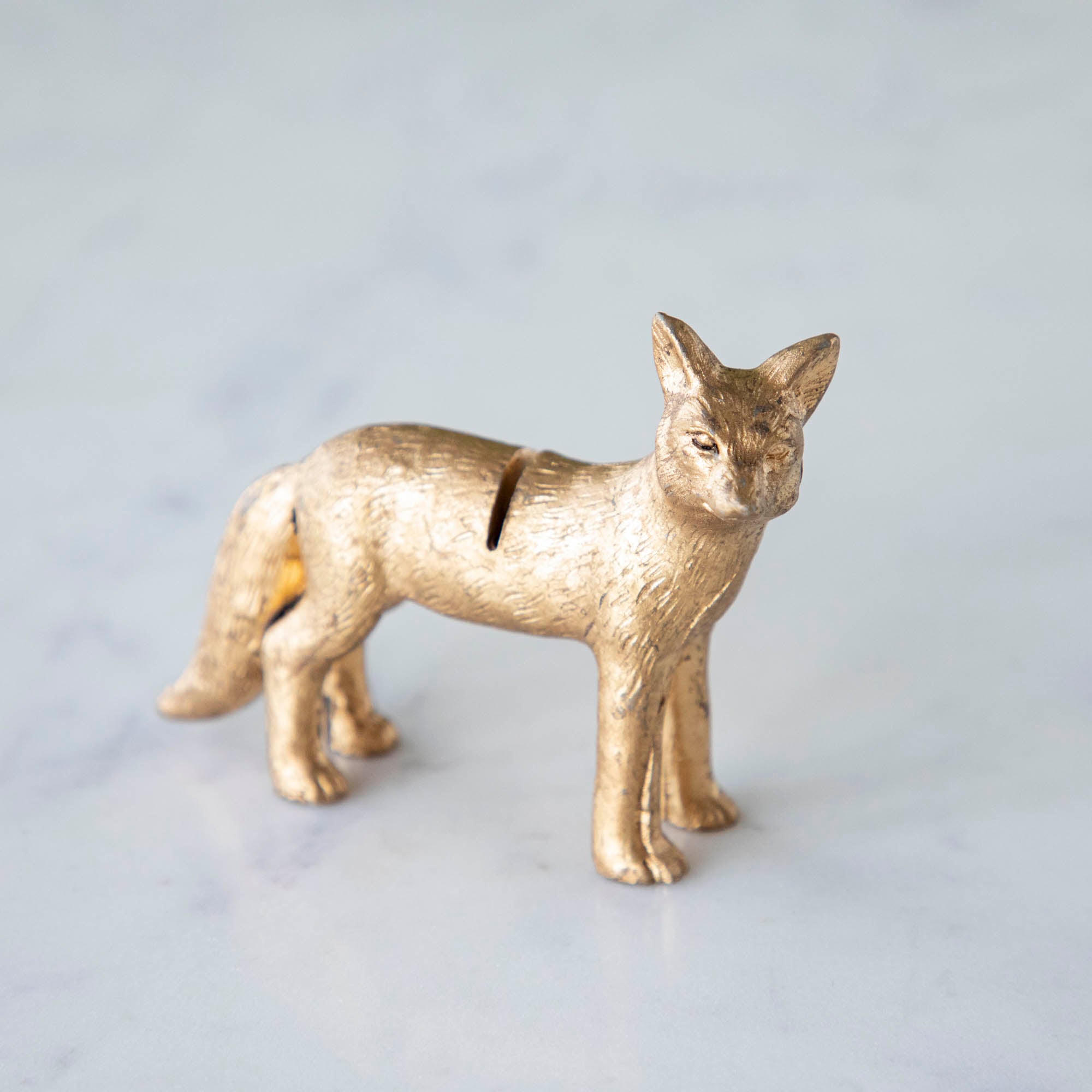 A side view of the Fox Name Card Holder, showing its tail and slot in its back, on a marble table.