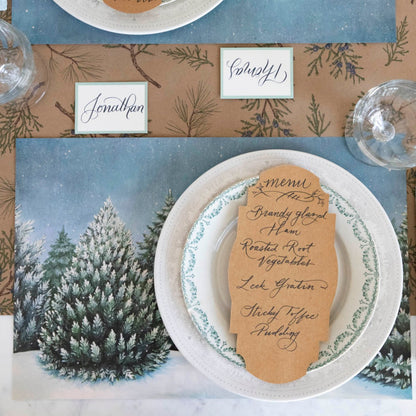 Evergreen Forest Placemat with white plates and a Kraft French Frame table card with a menu written on it and a Juniper Sprigs runner underneath.