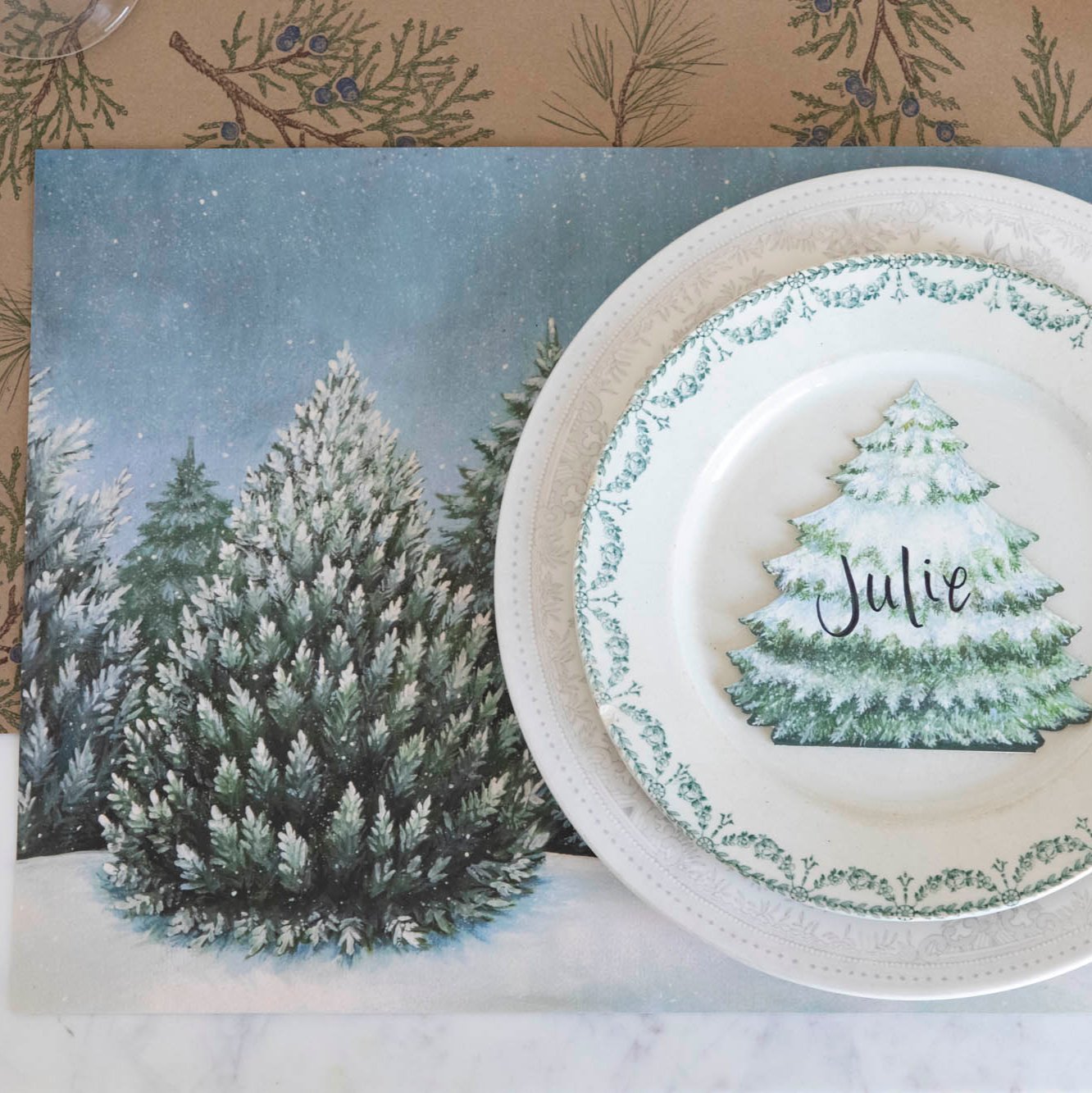 Evergreen Forest Placemat with white dinner plates and an Evergreen place card with the name &quot;Julie&quot; written on it and a Juniper Sprigs runner underneath. 