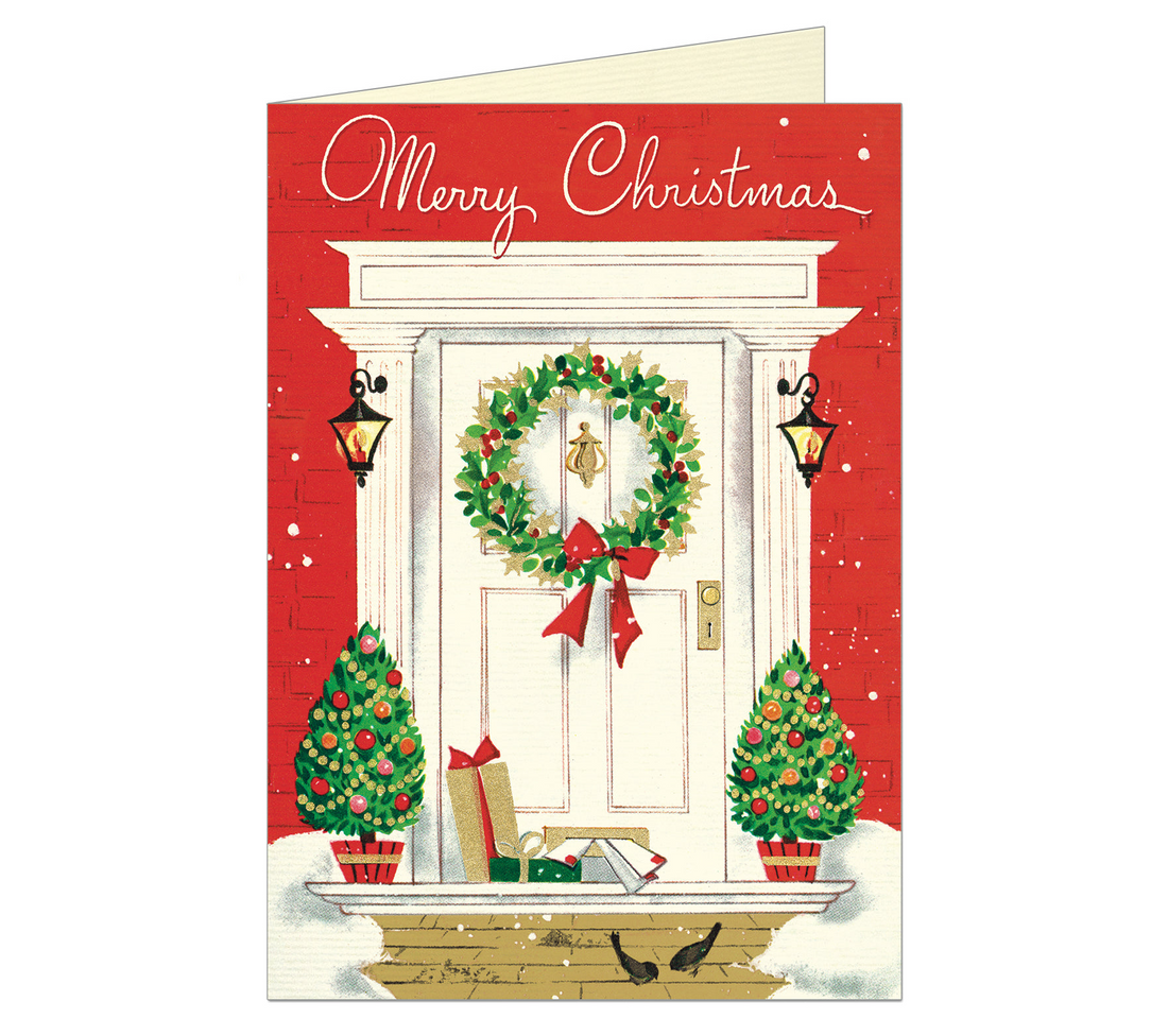 Greeting card with a drawing of a red brick house and its white front door with a wreath on it and packages in front of it saying Merry Christmas in script. 