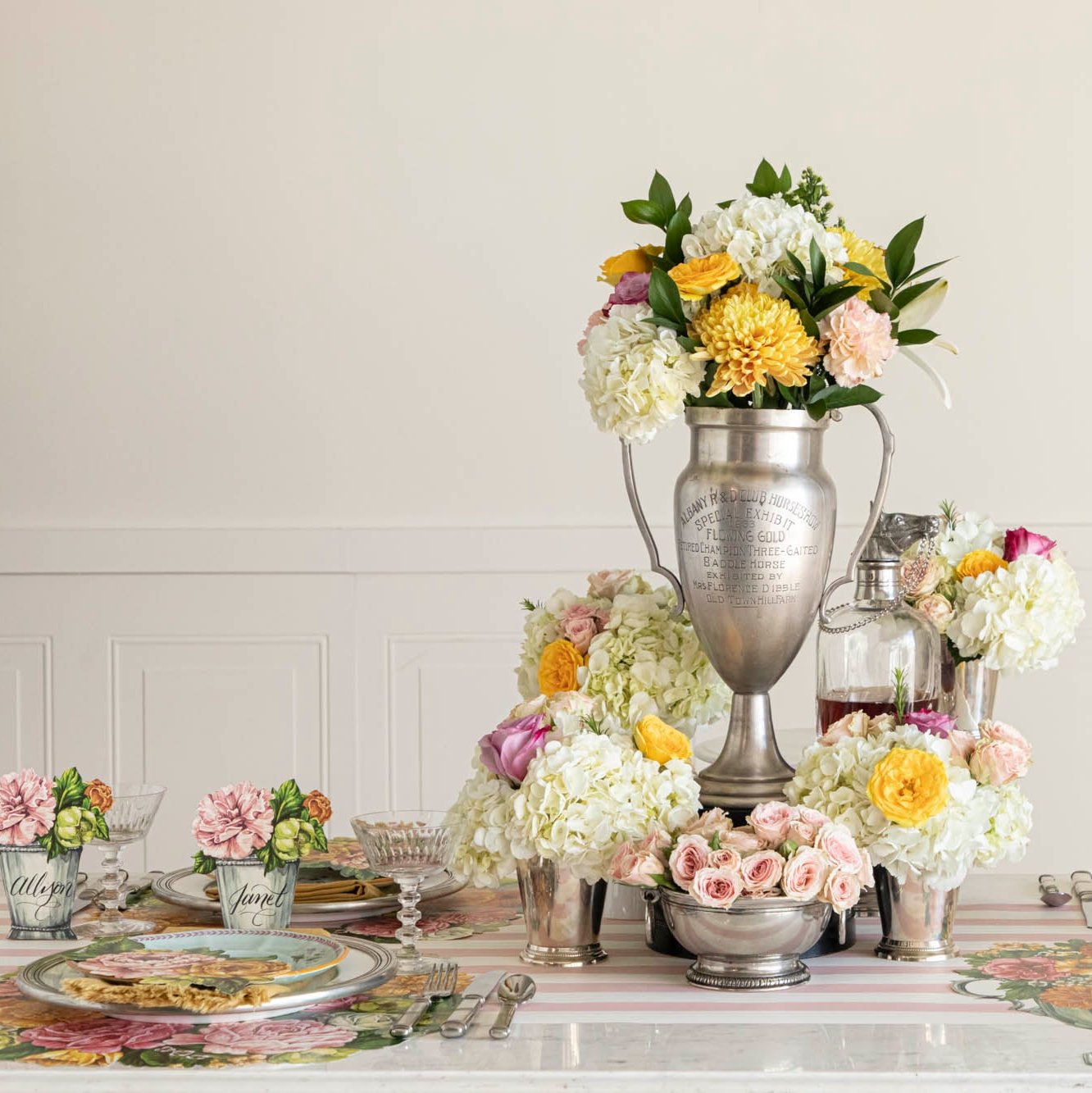 The Die-cut Derby Wreath Placemat Placemat in an elegant table setting for four, featuring a silver trophy in the floral centerpiece.