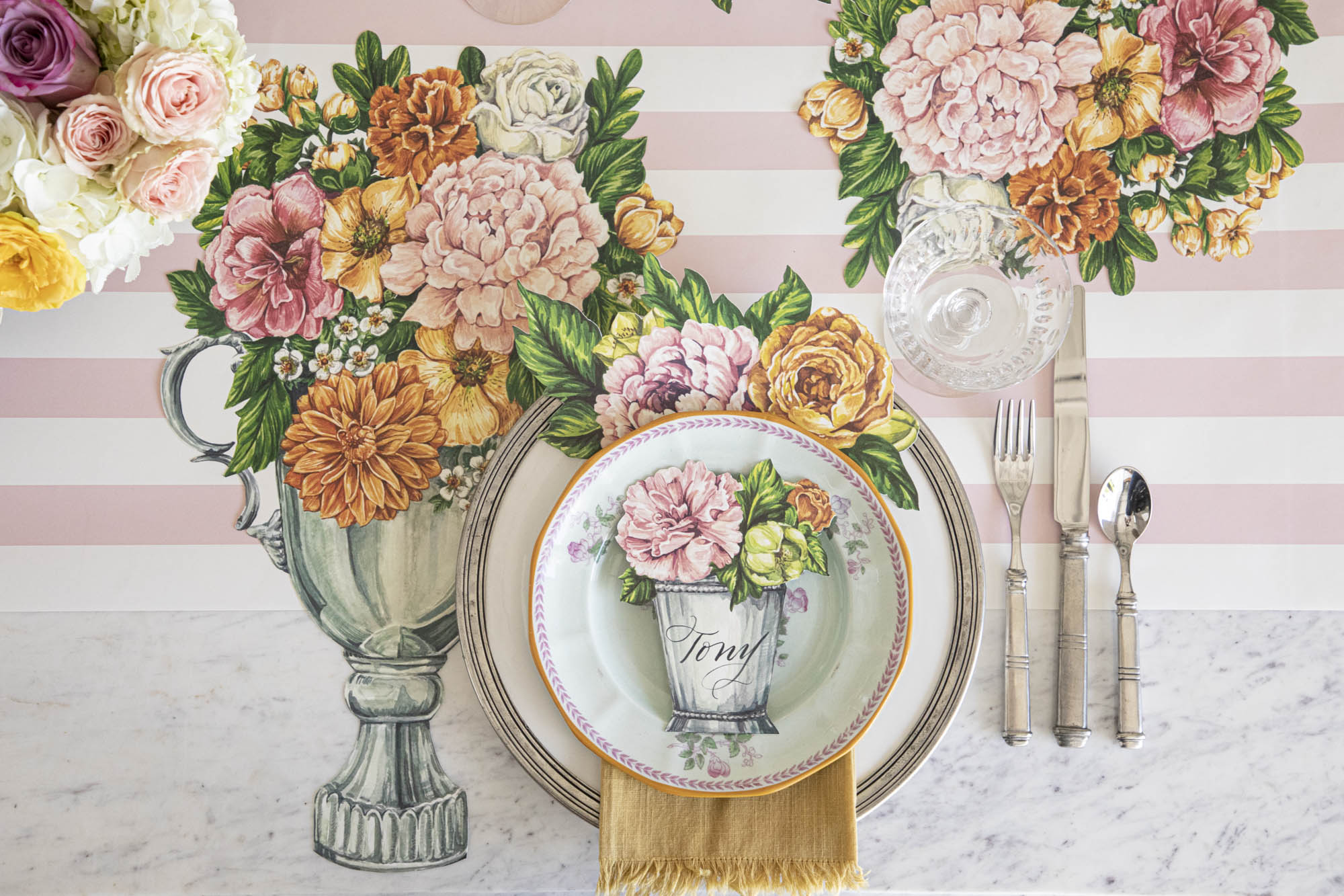 Top-down view of an elegant floral place setting featuring a Garden Derby Place Card labeled &quot;Tony&quot; laying flat on the plate.