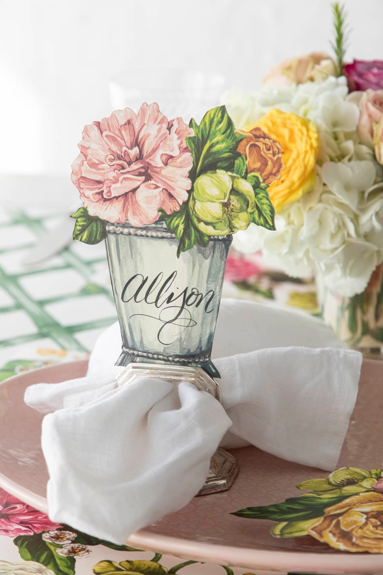 A Garden Derby Place Card labeled &quot;Allison&quot; on a place card holder napkin ring on the plate of an elegant place setting.