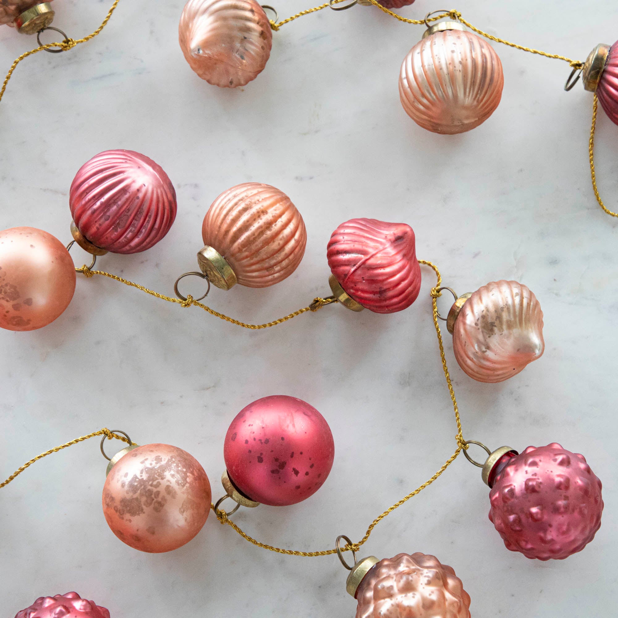 Close up view of the Embossed Mercury Glass Ball Ornament Pink Garland showing various pinks and details in the ornaments strung on a gold jute cord.