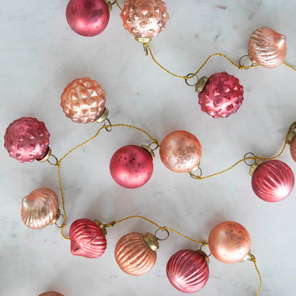 Close up view of the Embossed Mercury Glass Ball Ornament Pink Garland showing various pinks and details in the ornaments strung on a gold jute cord.