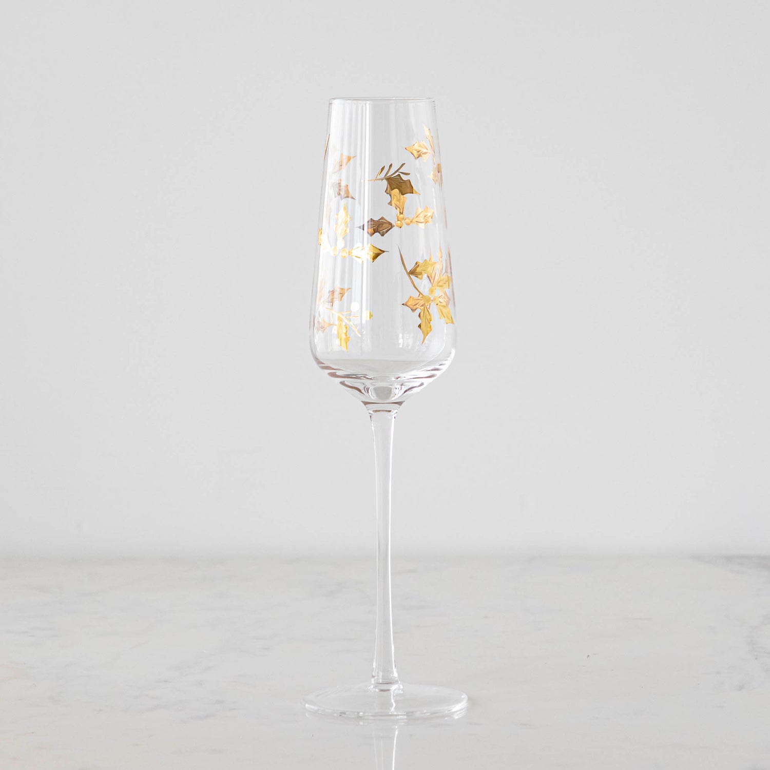 A Gold Holly Etched Flute glass on a marble table.