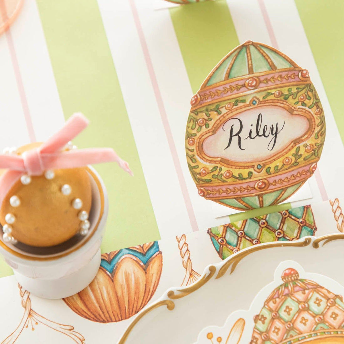 The Exquisite Egg Place Card with &quot;Riley&quot; written on it, next to a decorated egg, on an elegant table setting.