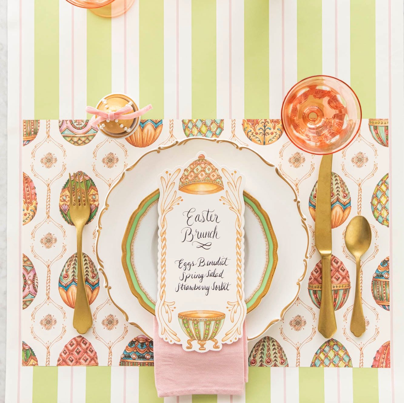 An elegant, Faberge Egg themed table setting, featuring the Exquisite Egg Hunt Placemat, Exquisite Egg Table Card with a menu written on it, and the Green &amp; Pink Awning Stripe Runner underneath.