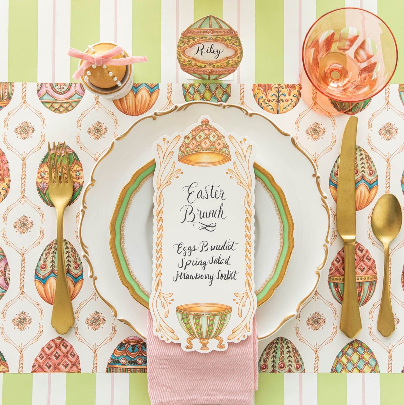 An elegant, Faberge Egg themed table setting, featuring the Exquisite Egg Hunt Placemat, Exquisite Egg Table Card with a menu written on it, and the Green &amp; Pink Awning Stripe Runner underneath.