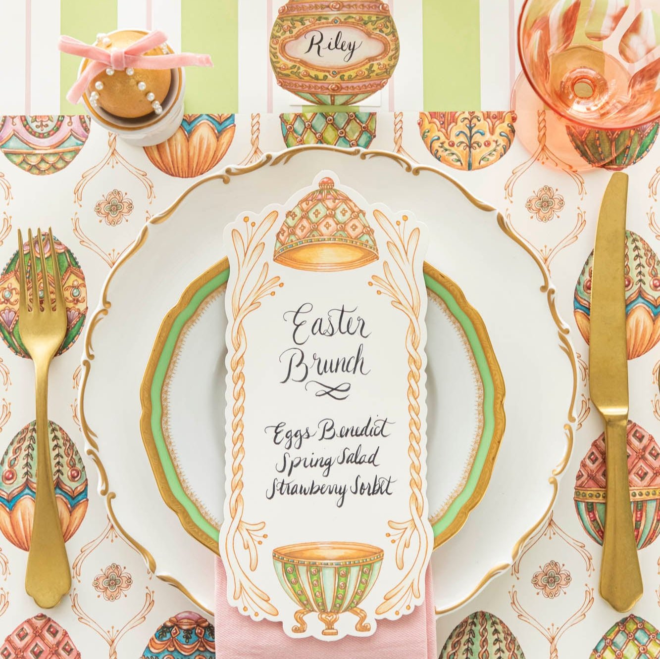 An elegant, Faberge Egg themed table setting, featuring the Exquisite Egg Hunt Placemat, Exquisite Egg Table Card with a menu written on it, and the Green &amp; Pink Awning Stripe Runner underneath.