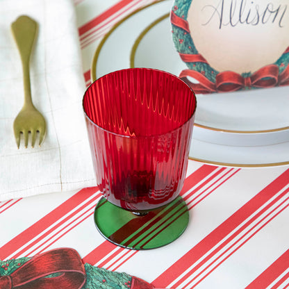 A green &amp; red stemmed flute glass on a red &amp; white striped runner.