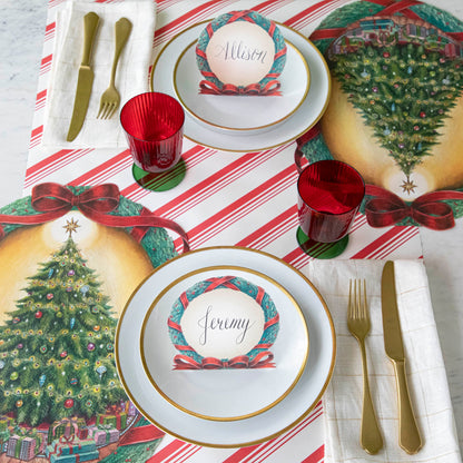 A Christmas themed table setting with plates, silverware and red &amp; green stemmed flute glasses.