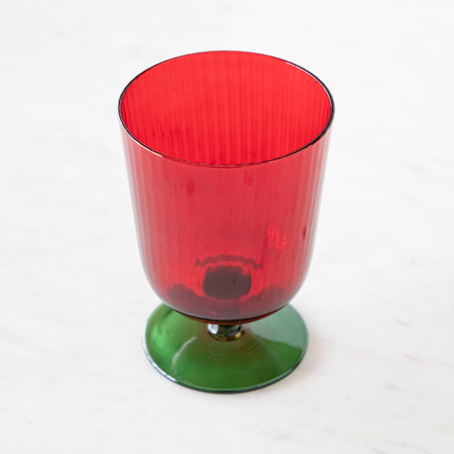 Inside view of a green &amp; red stemmed flute glass on a marble table.