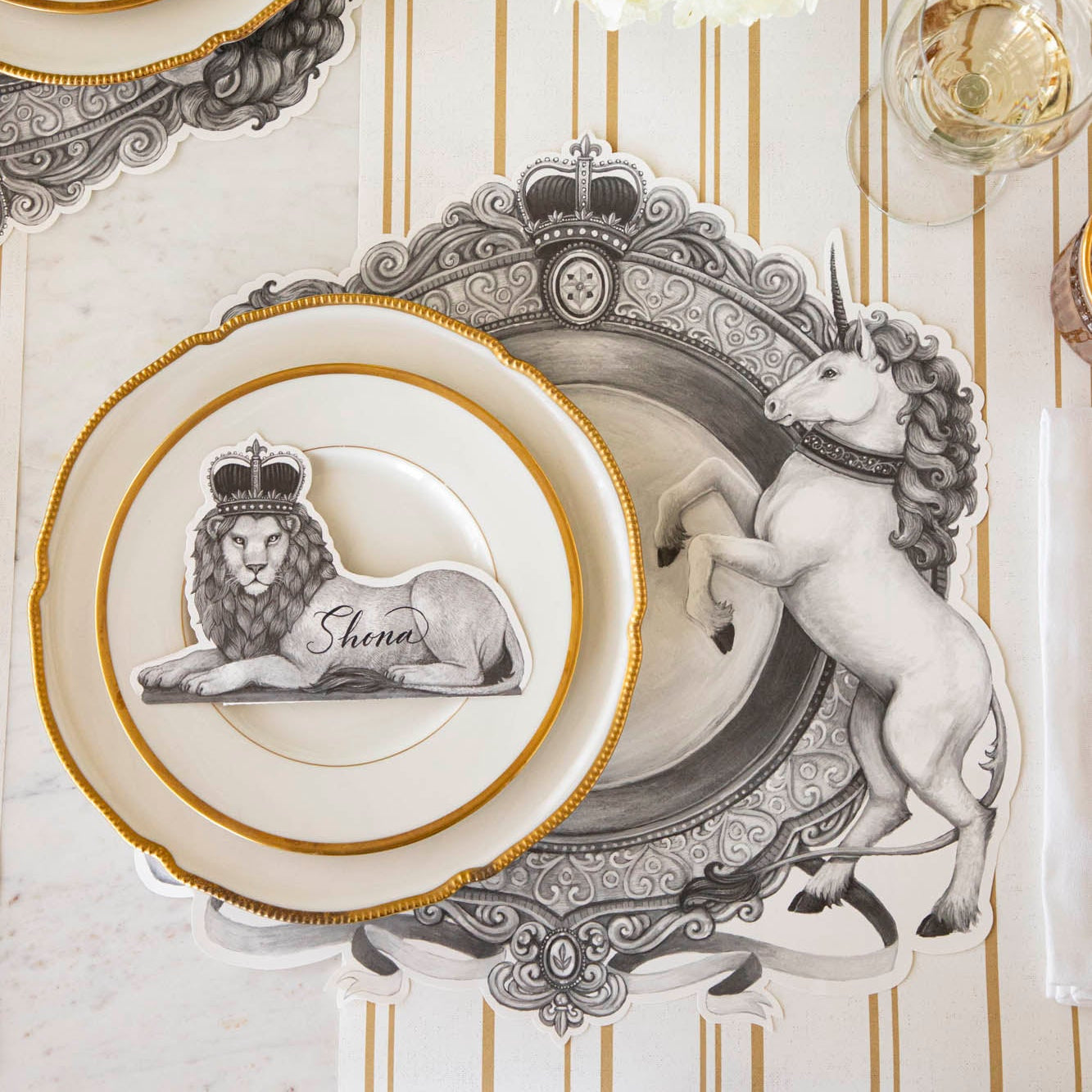 Regal Lion Place Card with &quot;Shona&quot; written on it, resting on dinner plates on top of the H&amp;C Regal Crest Placemat.