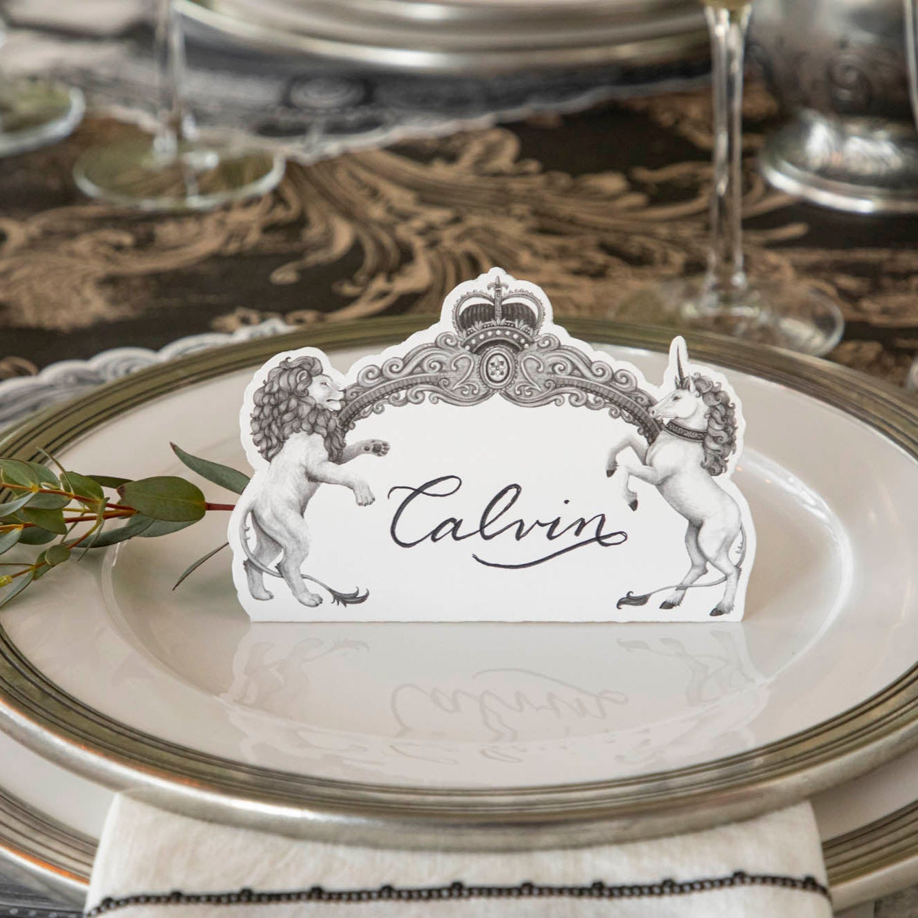 Regal Crest Place Card with &quot;Calvin&quot; written on it, resting on dinner plates, on a table setting for one.