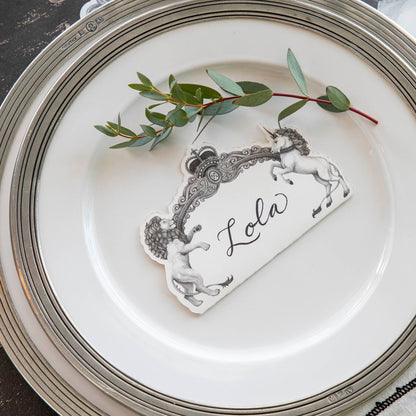 Regal Crest Place Card with &quot;Lola&quot; written on it, laying flat on dinner plates next to a small decorative branch.