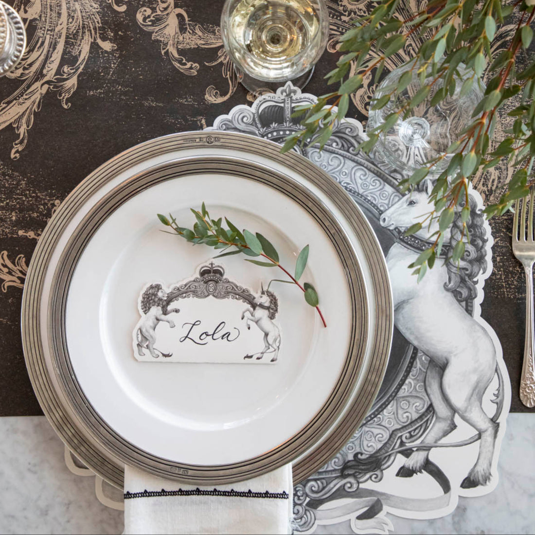 Regal Crest Place Card with &quot;Lola&quot; written on it, resting on dinner plates, on a table setting for one.